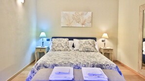 A neatly arranged bedroom with a large bed, two bedside tables with lamps, and a floral artwork on the wall.