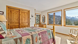 A bedroom with a large bed, wooden wardrobe, dresser, and a view of mountains through a window. - Dances With Wolves Vacation At Windcliff 3 Bedroom Home by RedAwning (Estes Park)