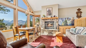 A living room with a stone fireplace, a dining area, and a large TV. - Dances With Wolves Vacation At Windcliff 3 Bedroom Home by RedAwning (Estes Park)