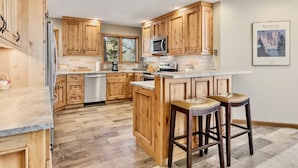 A kitchen with wooden cabinets, a microwave, and a large island with stools. - Dances With Wolves Vacation At Windcliff 3 Bedroom Home by RedAwning (Estes Park)