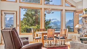 A cozy room with a dining table, chairs, and a sofa. Large windows offer a view of mountains and trees. - Dances With Wolves Vacation At Windcliff 3 Bedroom Home by RedAwning (Estes Park)