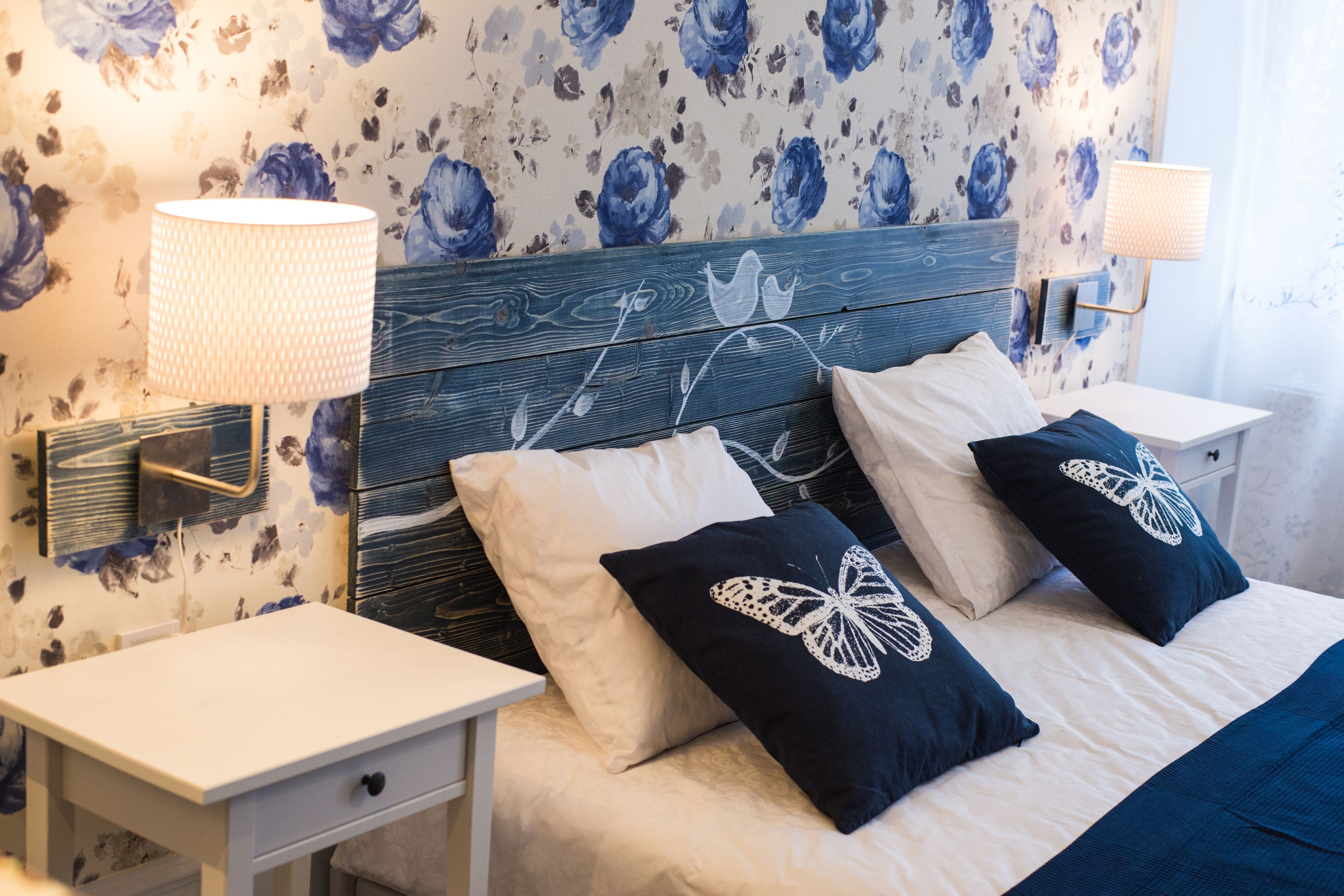 A bedroom with a wooden headboard, two bedside tables with lamps, a bed with a white and blue bedspread, and decorative pillows.