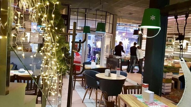 An indoor dining area with tables and chairs, a counter with a person behind it, and decorative lights. - Central Hotel (Lviv)
