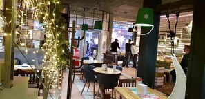 An indoor dining area with tables and chairs, a counter with a person behind it, and decorative lights. - Central Hotel (Lviv)