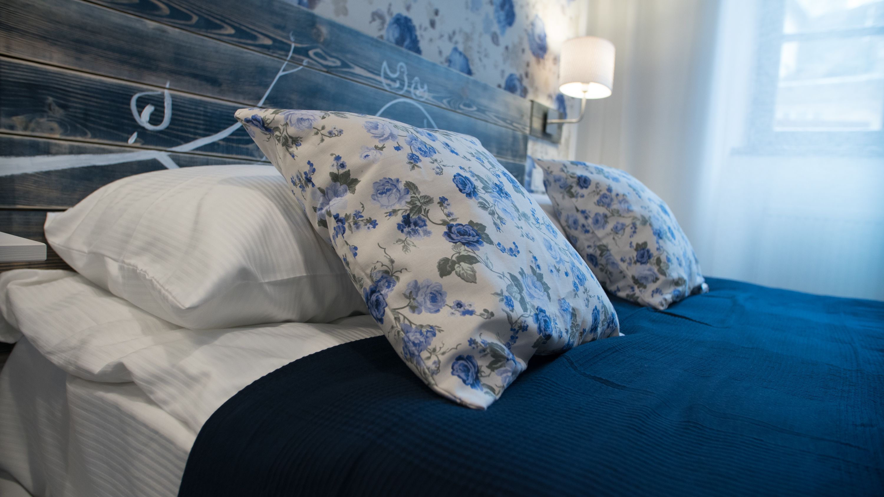 A bed with white and blue floral pillows, a dark blue bedspread, and a wooden headboard with a floral pattern.