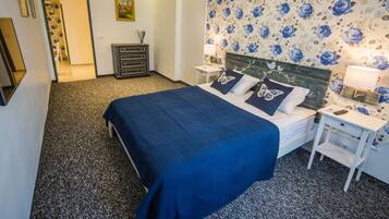 A bedroom with a bed, nightstands, a dresser, and a floral wallpaper.