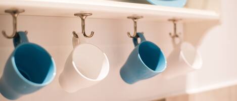 A kitchen with a white shelf holding blue and white mugs and plates.