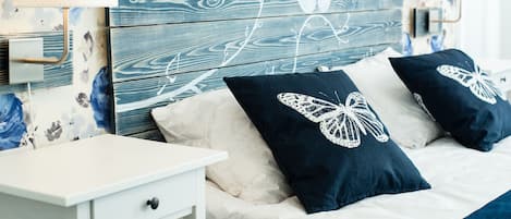 Un dormitorio con cabecera de madera, dos mesitas de noche, una cama con almohadas azul oscuro y papel tapiz floral.