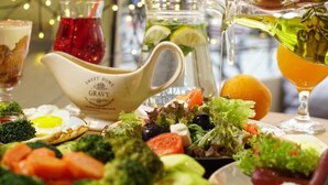 A table set with various dishes, including a salad, a pitcher of gravy, and a glass of a yellow beverage. - Central Hotel (Lviv)