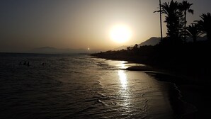 A beach at sunset with calm waters, palm trees, and distant mountains. - Beachfront Newly Renovated Duplex with Sea Views (Marbella)