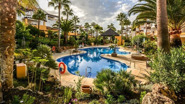 A swimming pool surrounded by palm trees and greenery, with a lifeguard stand and lounge chairs. - Beachfront Newly Renovated Duplex with Sea Views (Marbella)