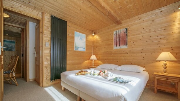A wooden cabin bedroom with a bed, two bedside lamps, a chair, and a painting on the wall. - Chalet Du Croz RJ Historic Farmhouse Charm, Sleeps 8, Le Tour (Argentière), France (Le Tour (Argentière))
