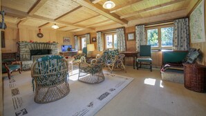 A cozy cabin interior with a stone fireplace, wicker chairs, a green sofa, and a large window. - Chalet Du Croz RJ Historic Farmhouse Charm, Sleeps 8, Le Tour (Argentière), France (Le Tour (Argentière))