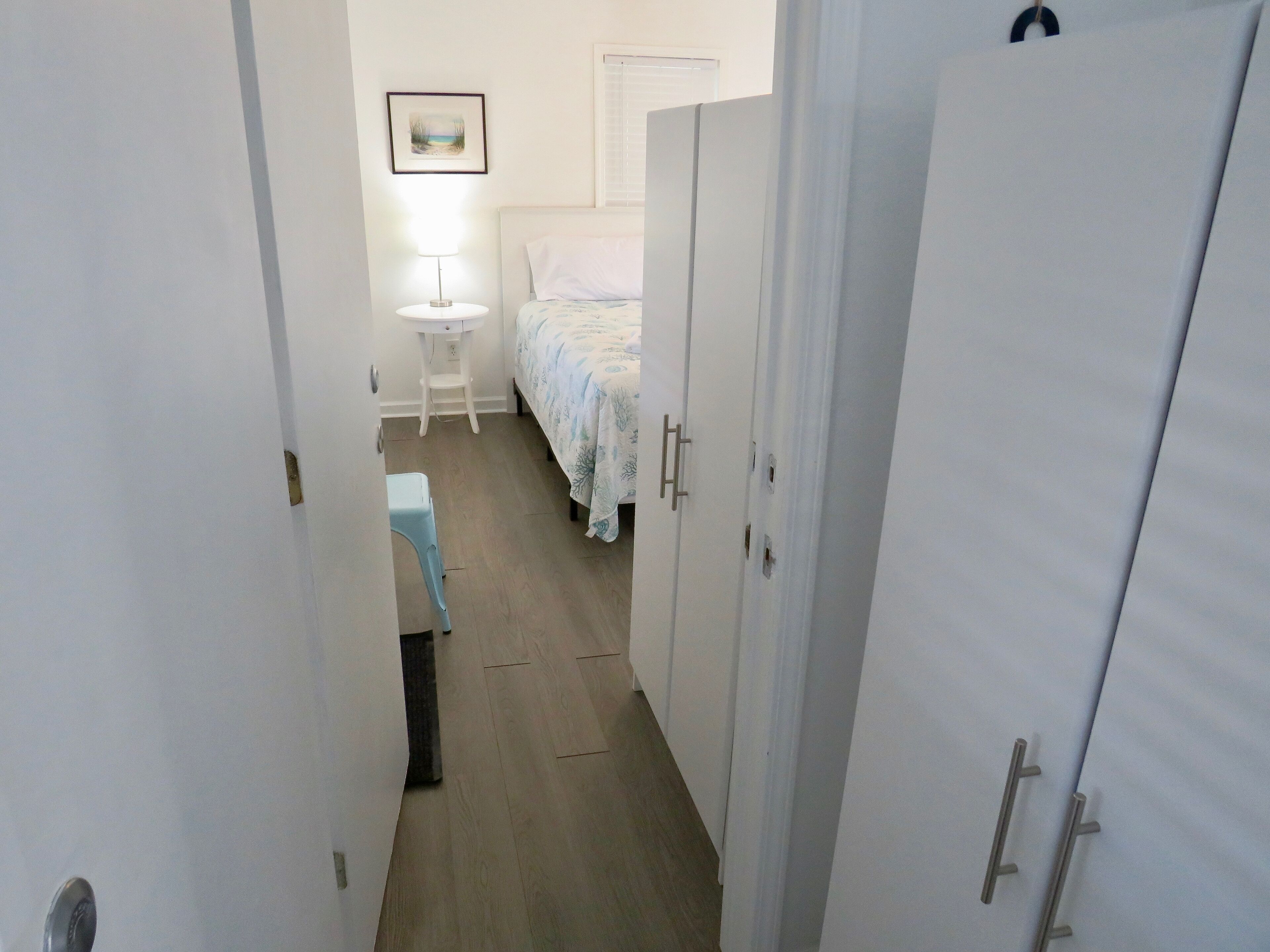 Um corredor estreito que leva a um quarto com uma cama, uma mesa de cabeceira e uma cadeira.