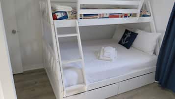 A bunk bed with a ladder, a white mattress, and a pillow with an anchor design.