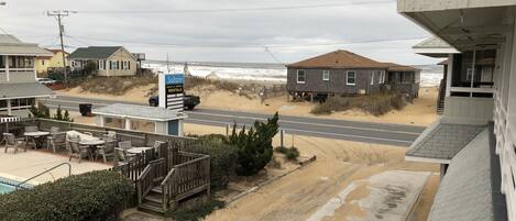 A beachfront property with a wooden deck and outdoor seating, a sign for 'Sailair Nightly Week Rentals', and a view of the beach and ocean.