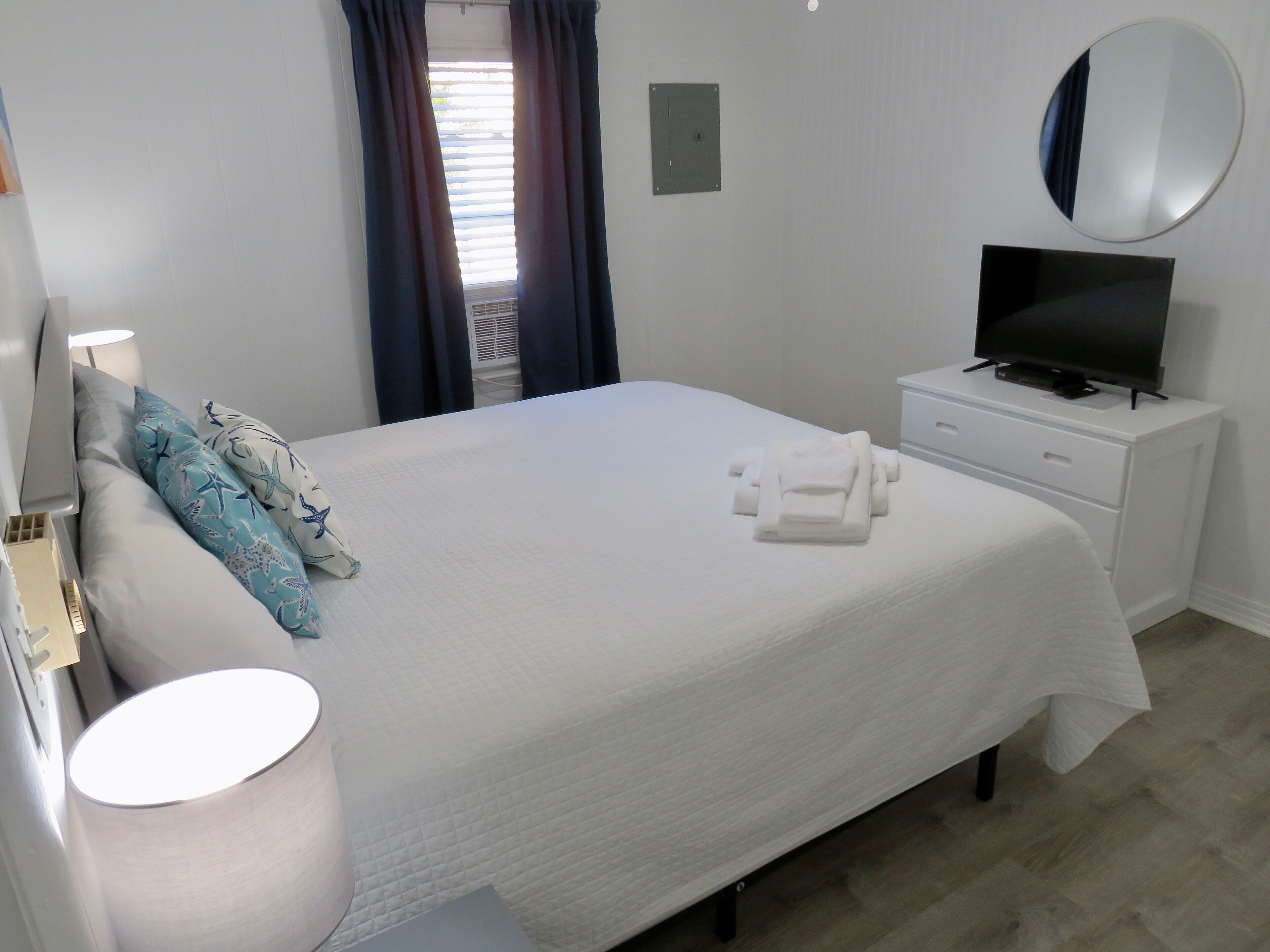 A hotel room with a bed, a TV, a bedside table, a lamp, and a window with curtains.