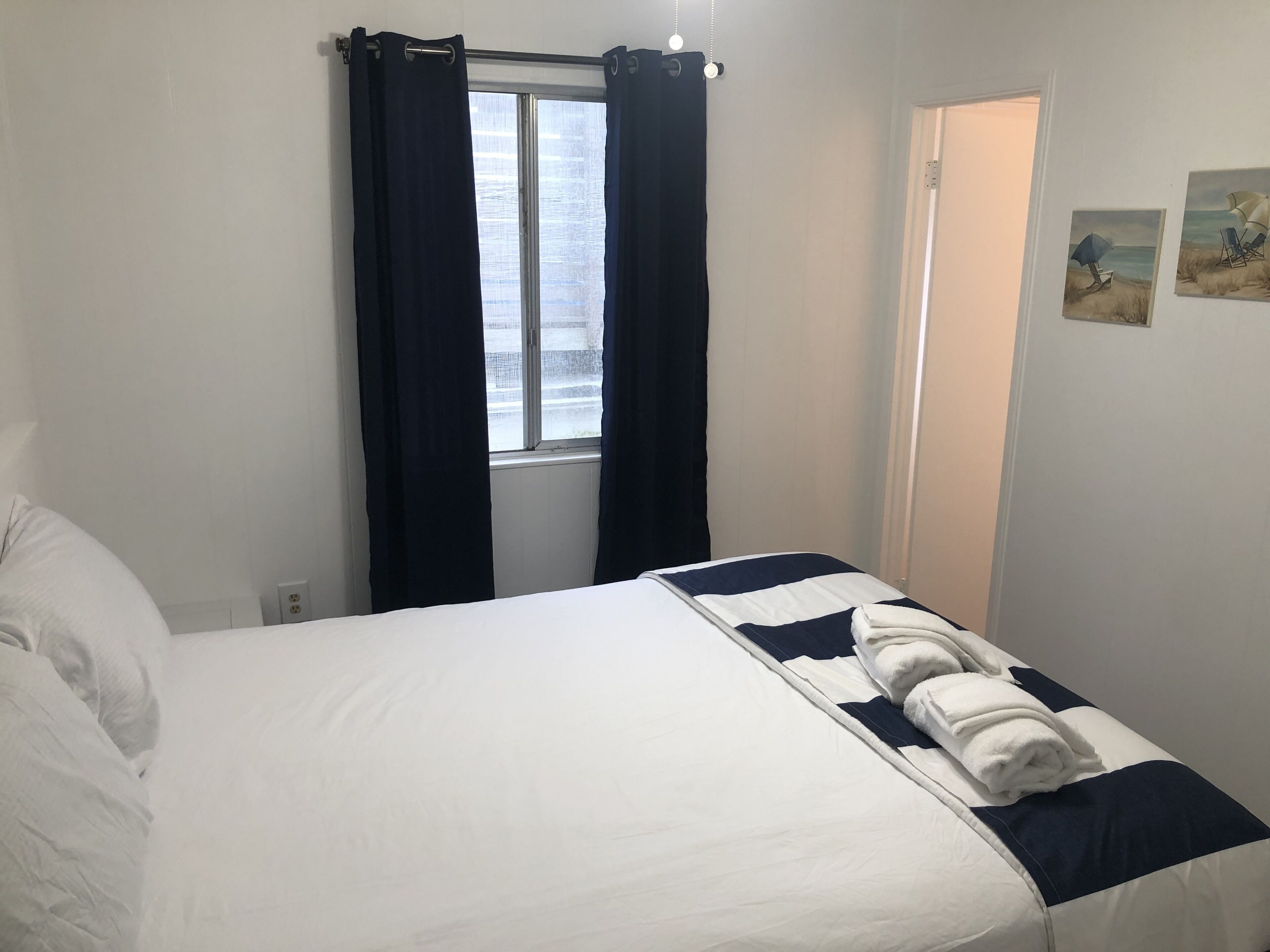 Une chambre à coucher avec un lit, une fenêtre avec des rideaux, une porte et un mur orné d’un tableau.