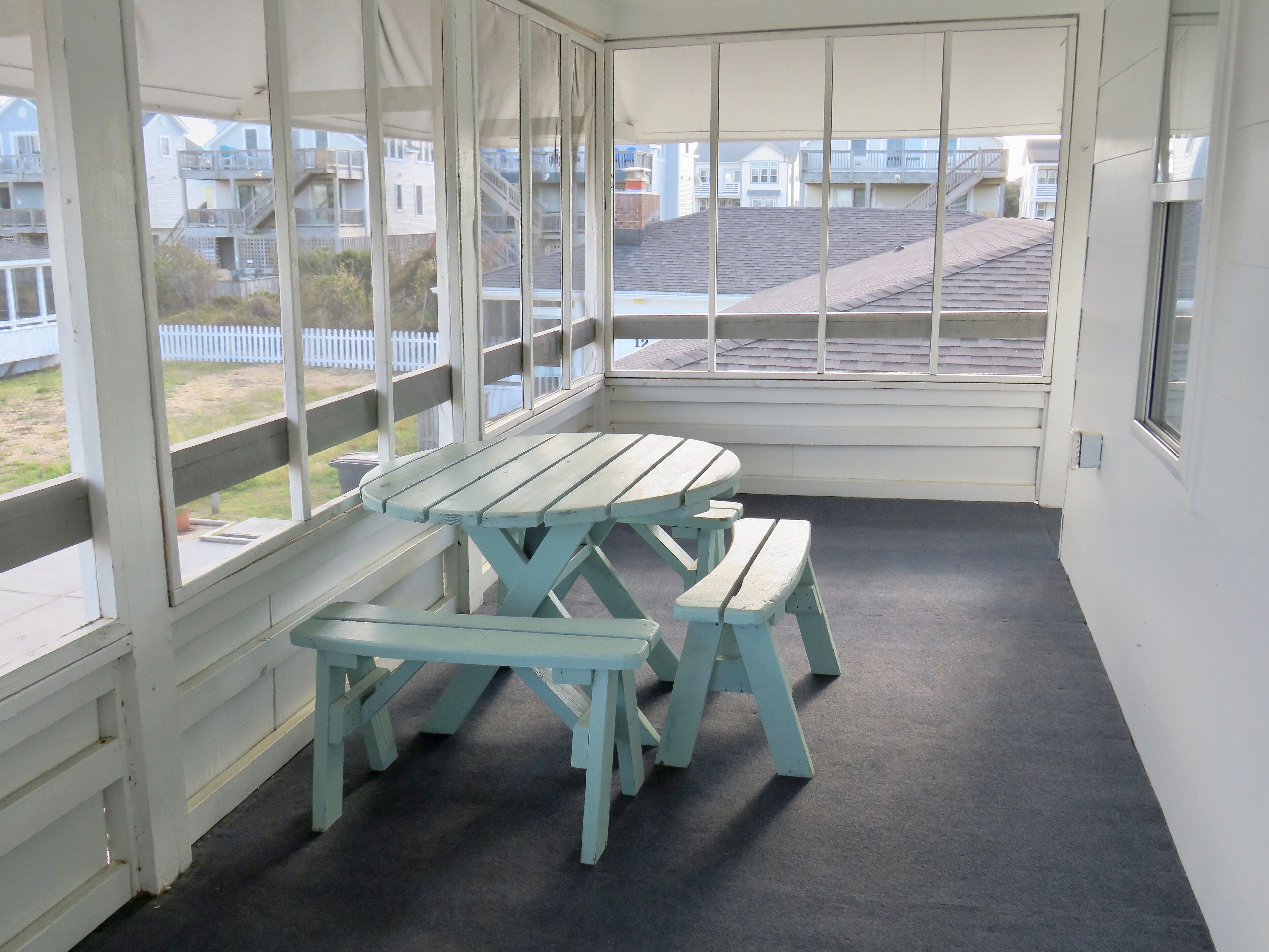 Een overdekt buitengebied met een picknicktafel en banken, grote ramen en uitzicht op woongebouwen.