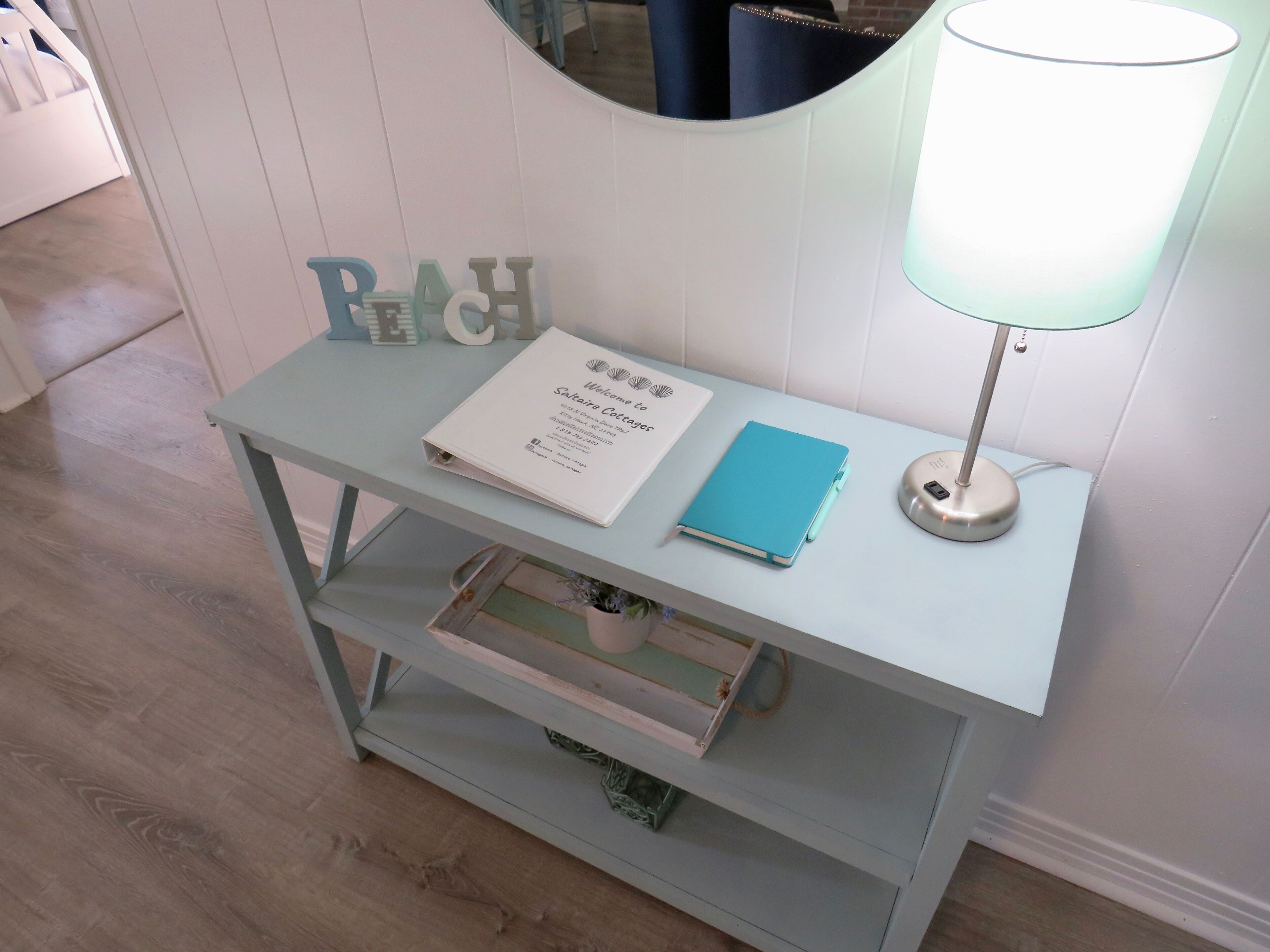 A light blue console table with a white sign, a blue notebook, and a lamp.