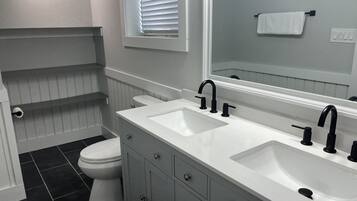 A bathroom with a white vanity, two sinks, a toilet, and a window with blinds.