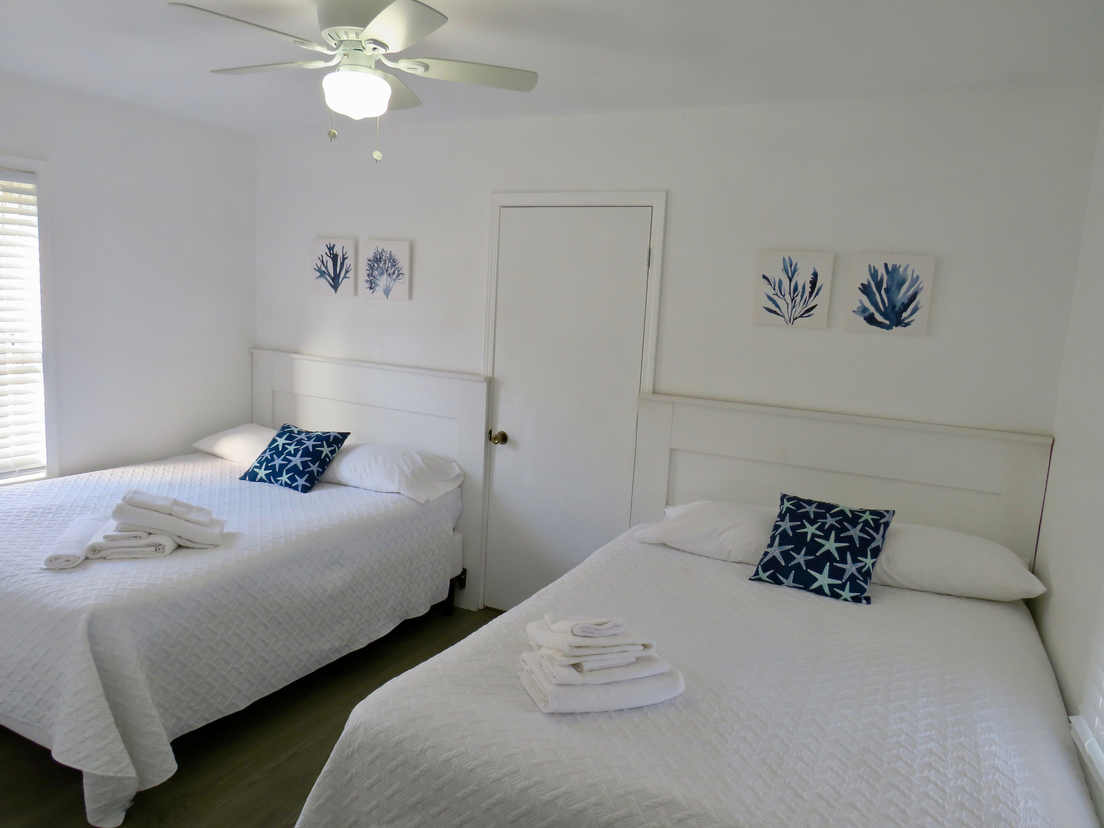 Habitación de hotel con dos camas, ropa de cama blanca y un ventilador de techo.