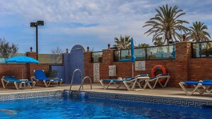 A swimming pool with blue water, surrounded by lounge chairs and palm trees.