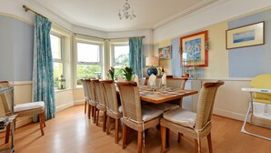 A dining area with a round table, wicker chairs, and a view of the outdoors through large windows. - GORGEOUS SPACIOUS  FAMILY HOUSE IN THE CENTRE OF ABERSOCH (Abersoch)