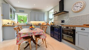 A kitchen with a dining table, chairs, a clock, and a view of the outdoors. - GORGEOUS SPACIOUS  FAMILY HOUSE IN THE CENTRE OF ABERSOCH (Abersoch)