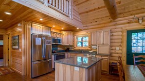 A log cabin kitchen with wooden cabinets, stainless steel appliances, a central island, and a window overlooking a rocky landscape. - Armstrong Luxury Log Vacation  At Windcliff 4 Bedroom Home by RedAwning (Estes Park)
