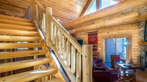 A wooden cabin interior with a wooden staircase, a fireplace, a sofa, and a dining table. - Armstrong Luxury Log Vacation  At Windcliff 4 Bedroom Home by RedAwning (Estes Park)