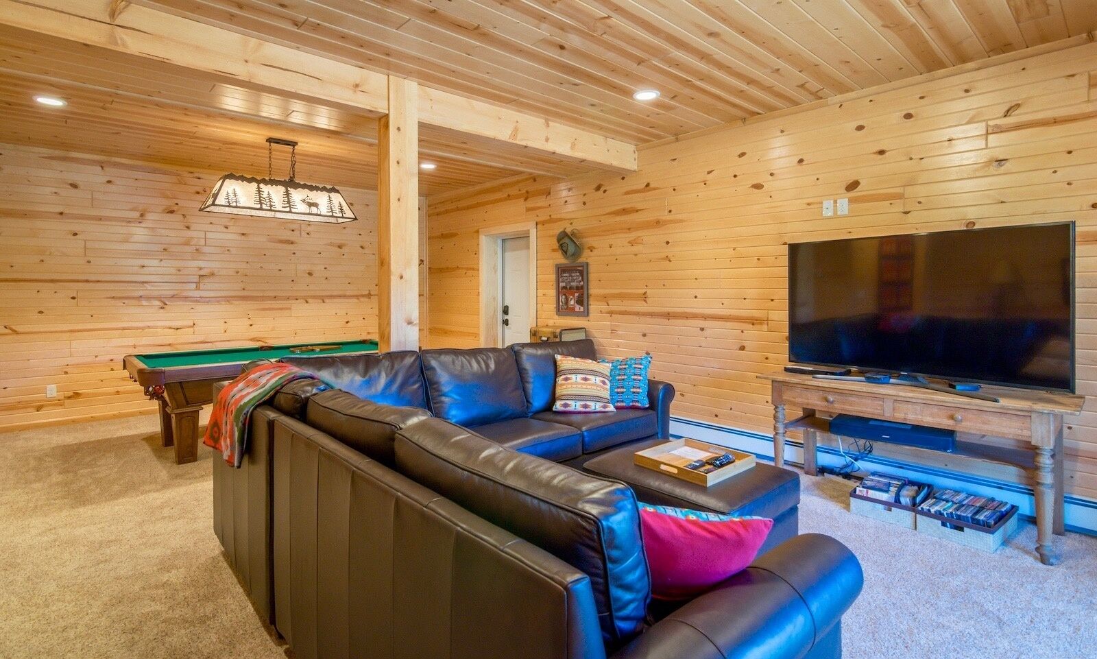 Ein gemütliches Wohnzimmer mit Billardtisch, einer Ledersofa, einem Fernseher und einer Holzbalkendecke.