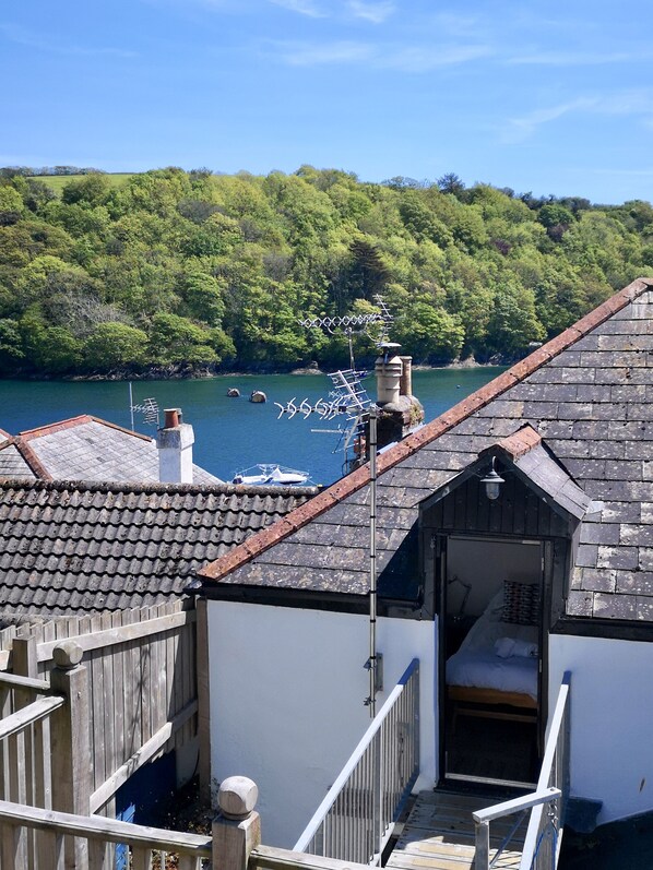 A coastal building with a tiled roof, a wooden deck, and a view of the sea and forested hills. - Modern Townhouse In Fowey, Cornwall, England (Fowey)