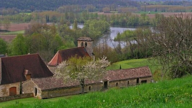 Un bâtiment historique, avec un toit recouvert de tuiles rouges, un clocher et une rivière en arrière-plan.
