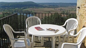Un balcon avec une table ronde et quatre chaises, offrant une vue panoramique sur un paysage pittoresque composé de champs et de collines.