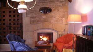 Une pièce chaleureuse avec une cheminée en pierre, deux fauteuils à motifs, une table en bois et un lampadaire.