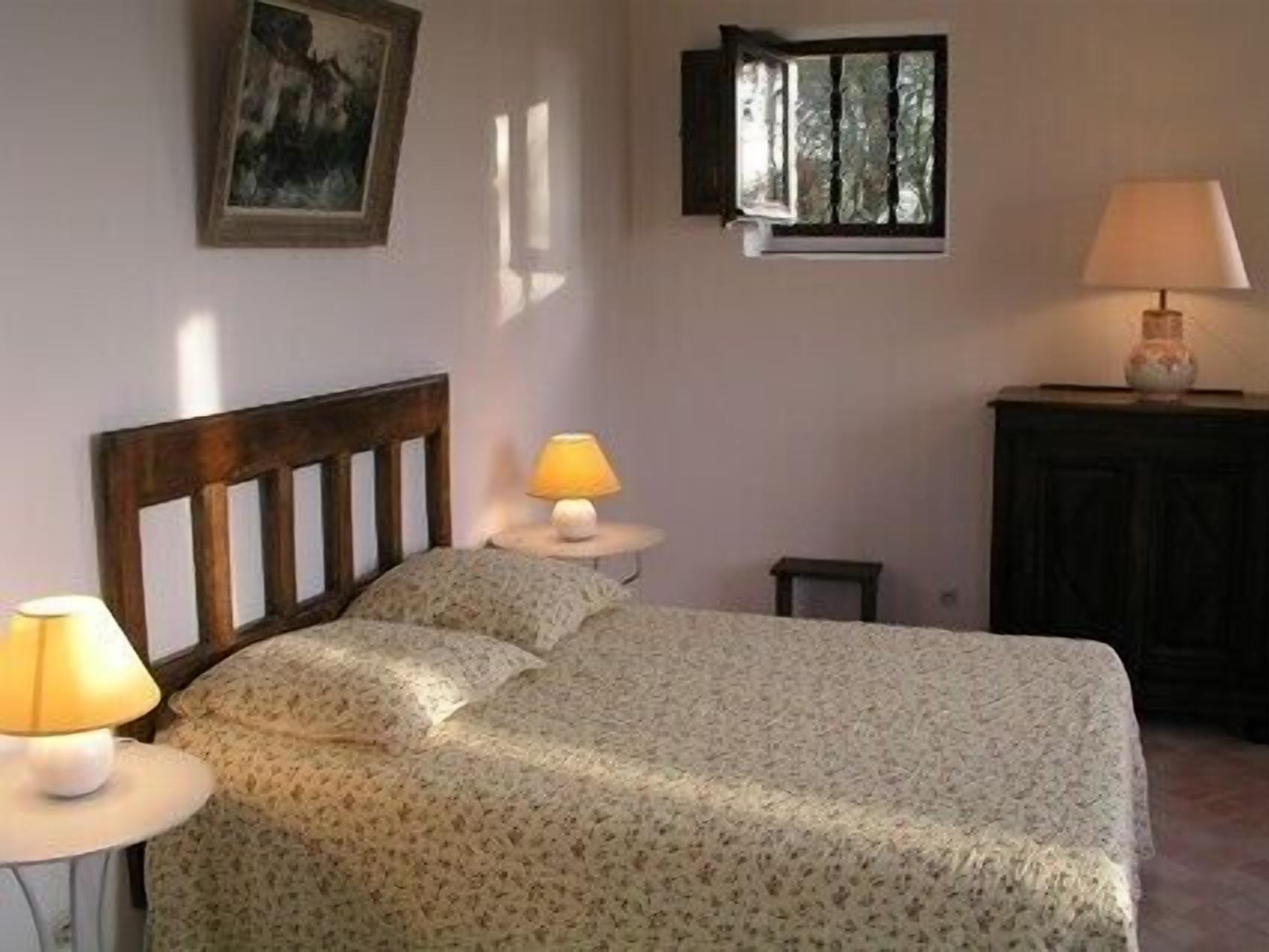 A bedroom with a bed, two bedside lamps, a nightstand, a small table, a cabinet, and a painting on the wall.