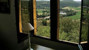 Une pièce dotée d’une grande fenêtre donnant sur un paysage verdoyant, avec des collines et une rivière.