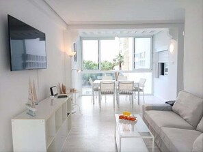 A modern living room with a sofa, coffee table, TV, and dining area.