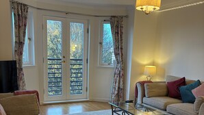 Una sala de estar con un sofá, una mesa de centro de vidrio, una lámpara y vistas a través de amplios ventanales.
