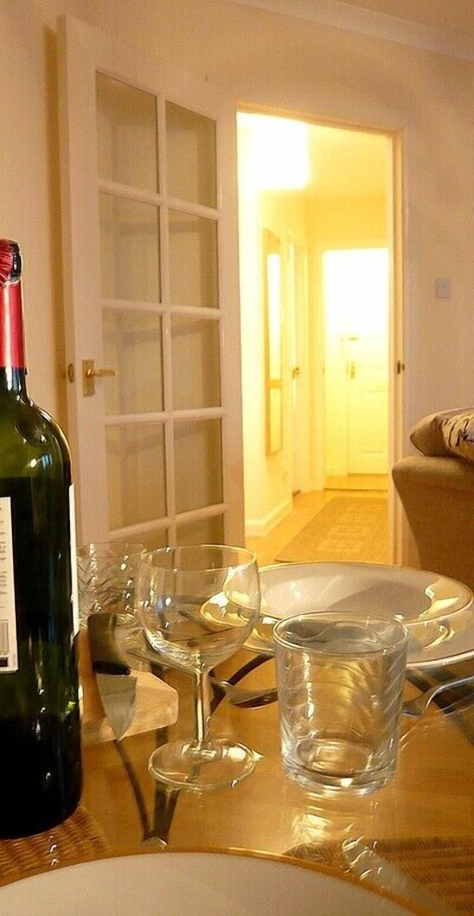 Une table à manger avec une bouteille de vin, plusieurs verres et des assiettes, ce qui laisse supposer qu’un repas va être servi.