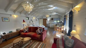 Ein geräumiger Wohnbereich mit einem roten Sofa, einem Holztisch und einer Chandelier. Im Hintergrund ist eine Küche mit einem Fenster und einem Esstisch zu sehen.