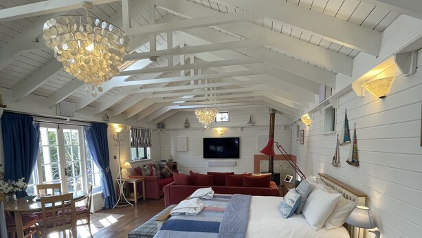 Ein geräumiges Schlafzimmer mit einem großen Bett, Holzboden, einer Kristallleuchtre, einem Fernseher und einer gemütlichen Sitzecke mit einem roten Sofa und einem kleinen Tisch.