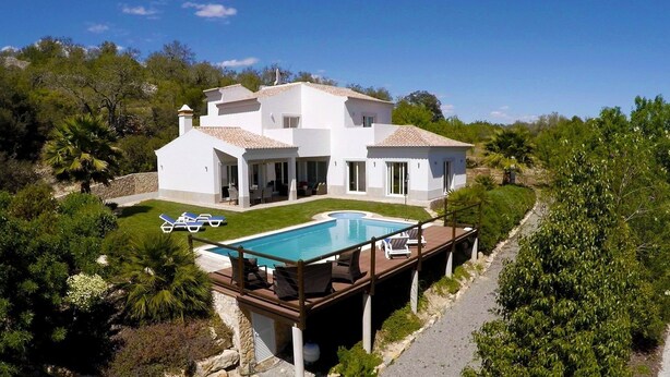Una villa blanca con piscina, rodeada de exuberante vegetación y árboles.