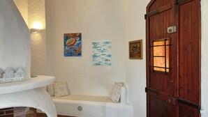 A room with a white bench, a wooden door, and wall art. - beautiful typical Sardinian villa 300 meters from the sea, 2 bedrooms, 2 bathro (La Ciaccia (Valledoria))