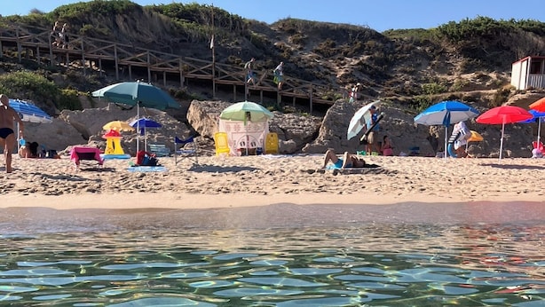 Clear water with visible sand patterns, beach umbrellas, and a rocky hillside in the background. - beautiful typical Sardinian villa 300 meters from the sea, 2 bedrooms, 2 bathro (La Ciaccia (Valledoria))