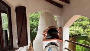 An outdoor dining area with a brick oven, white plastic chairs, and a table set with a tablecloth and plates. - beautiful typical Sardinian villa 300 meters from the sea, 2 bedrooms, 2 bathro (La Ciaccia (Valledoria))