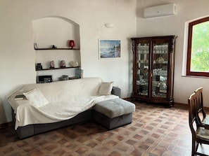 A living room with a sectional sofa, a cabinet with glass doors, a wall-mounted shelf, and a window. - beautiful typical Sardinian villa 300 meters from the sea, 2 bedrooms, 2 bathro (La Ciaccia (Valledoria))