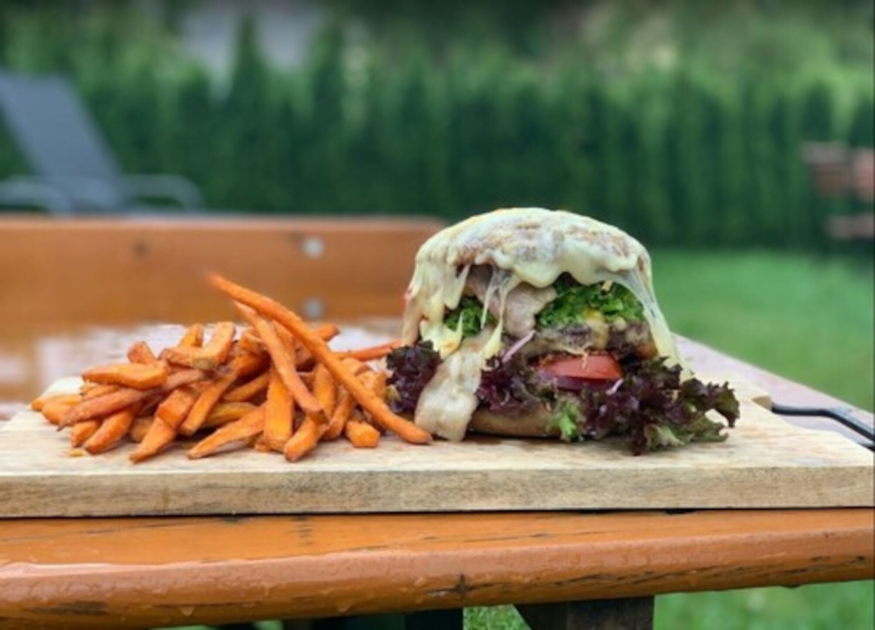 A burger with fries on a wooden table outdoors.