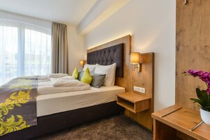 Habitación de hotel moderna con una cama grande, cabecera de madera, lámparas de noche, una mesita de noche de madera y una orquídea en maceta.
